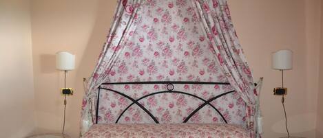 A bedroom with a canopy bed, two bedside tables, and a wall-mounted lamp.