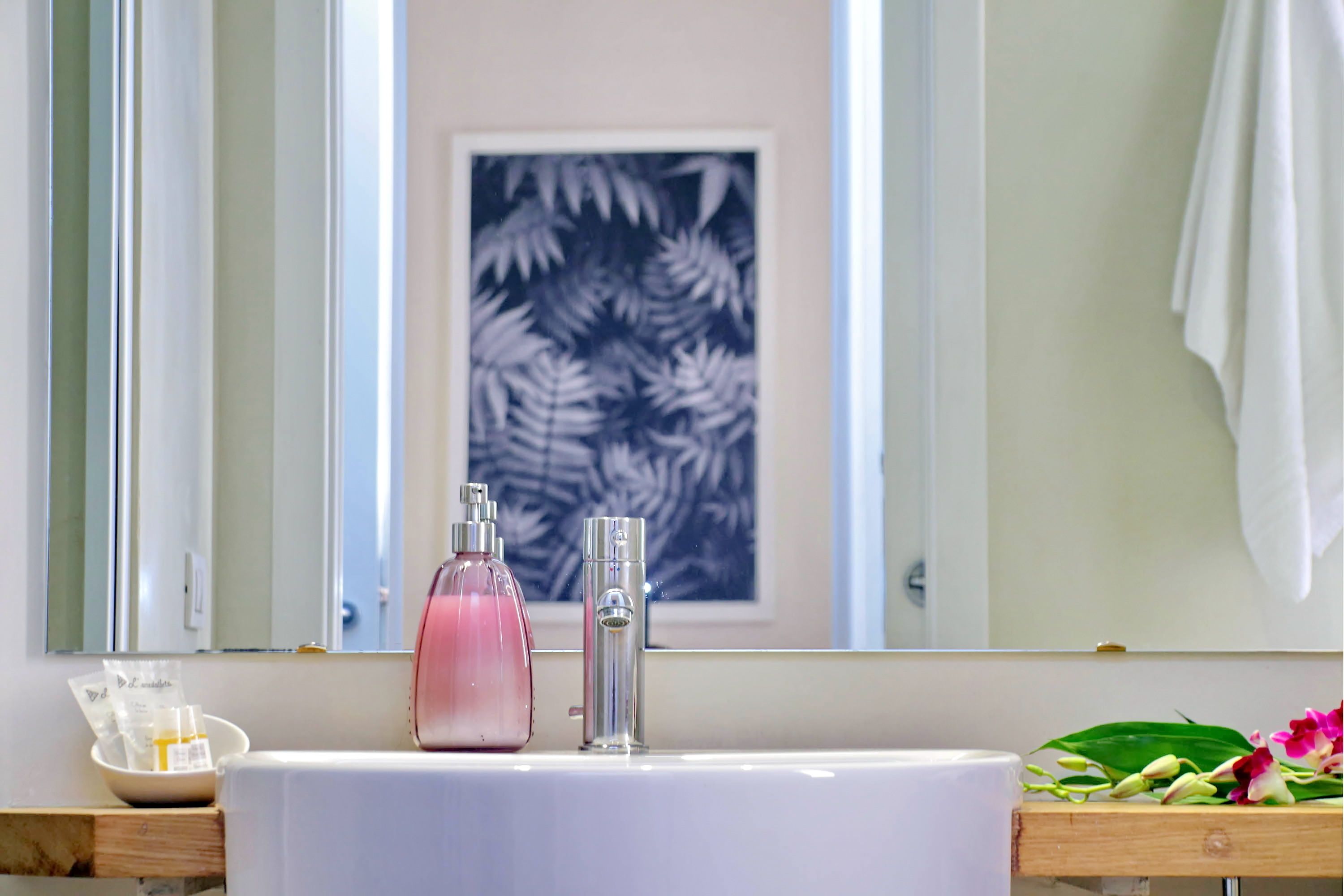 A bathroom with a white sink, a mirror, and a framed artwork of leaves on the wall.