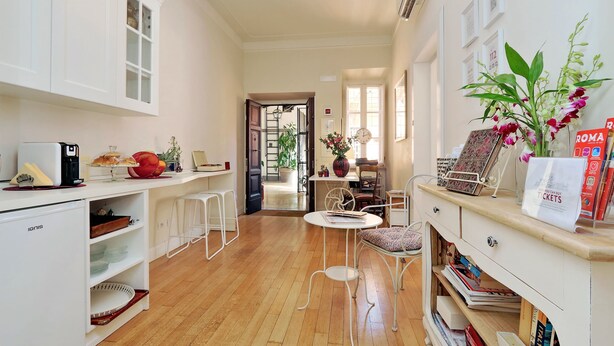 A compact kitchen with white cabinetry, a small refrigerator, and a dining area with a table and chairs. - Amaranto Romano (Rome)