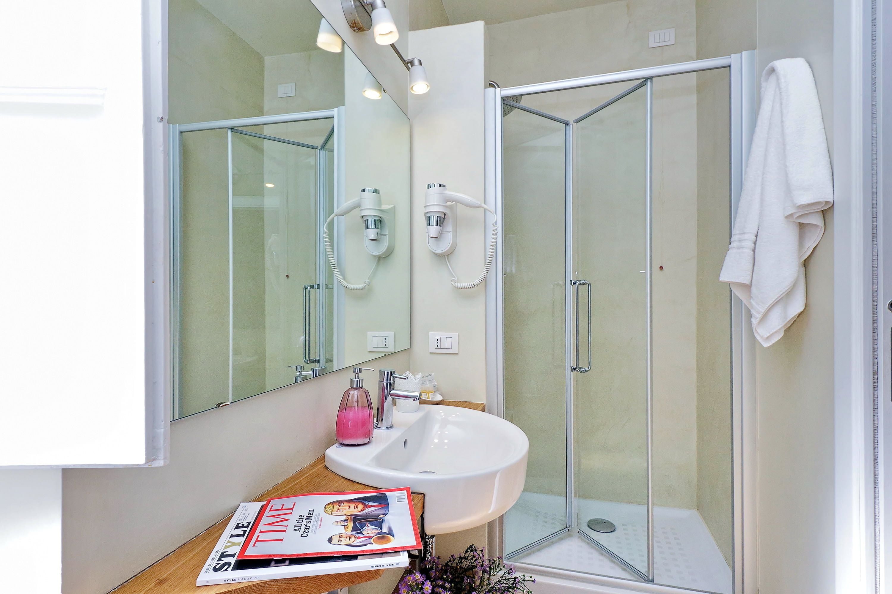A modern bathroom with a glass shower enclosure, a white sink, and a magazine on the counter.
