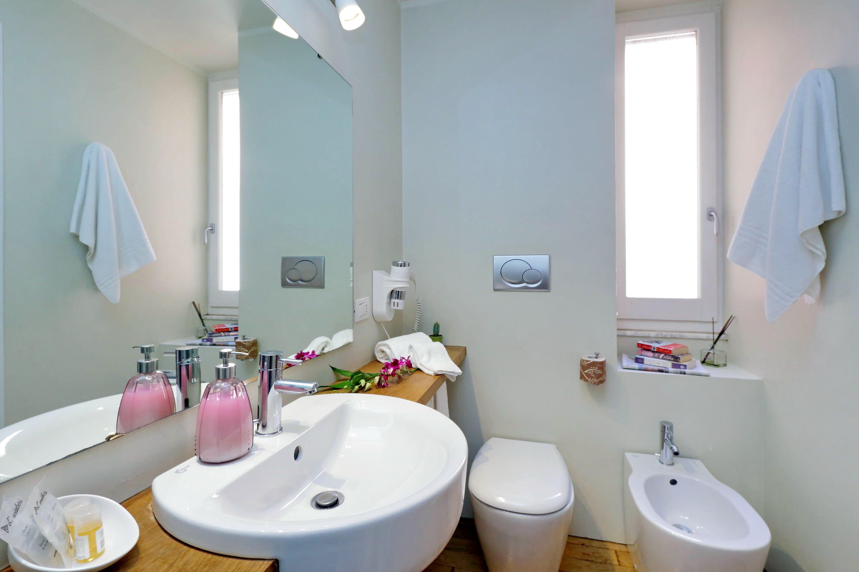 A modern bathroom with a large mirror, two sinks, a toilet, and a bidet.