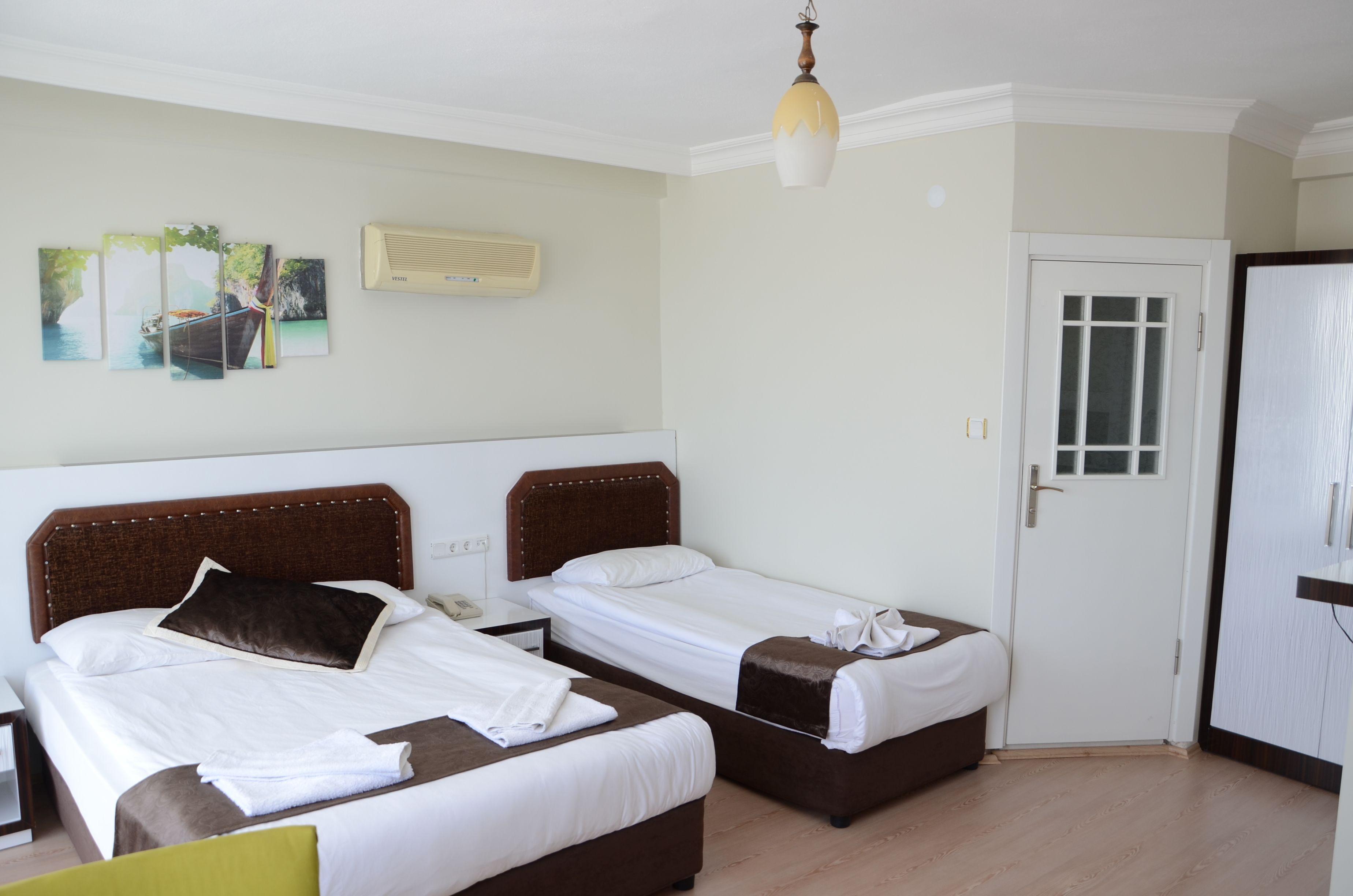 A hotel room with two beds, a wardrobe, a door, and a wall-mounted air conditioner.