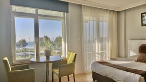 Ein Hotelzimmer mit einem Bett, einem runden Tisch mit Stühlen und großen Fenstern mit Blick auf das Meer und Palmen.
