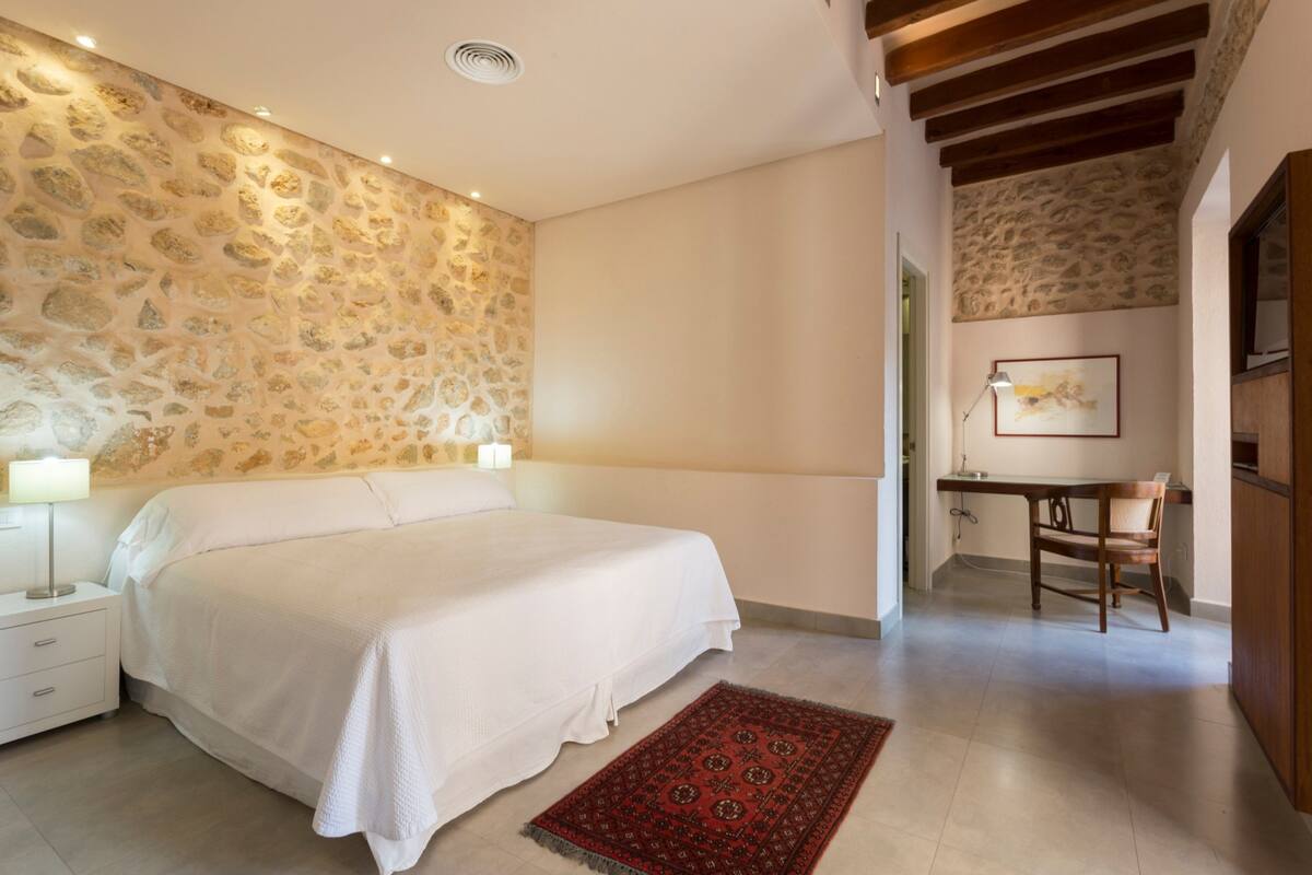 A bedroom with a stone wall, a bed, a desk, and a chair.