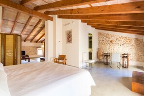 A spacious room with a large bed, wooden beams, stone walls, and a stone fireplace.