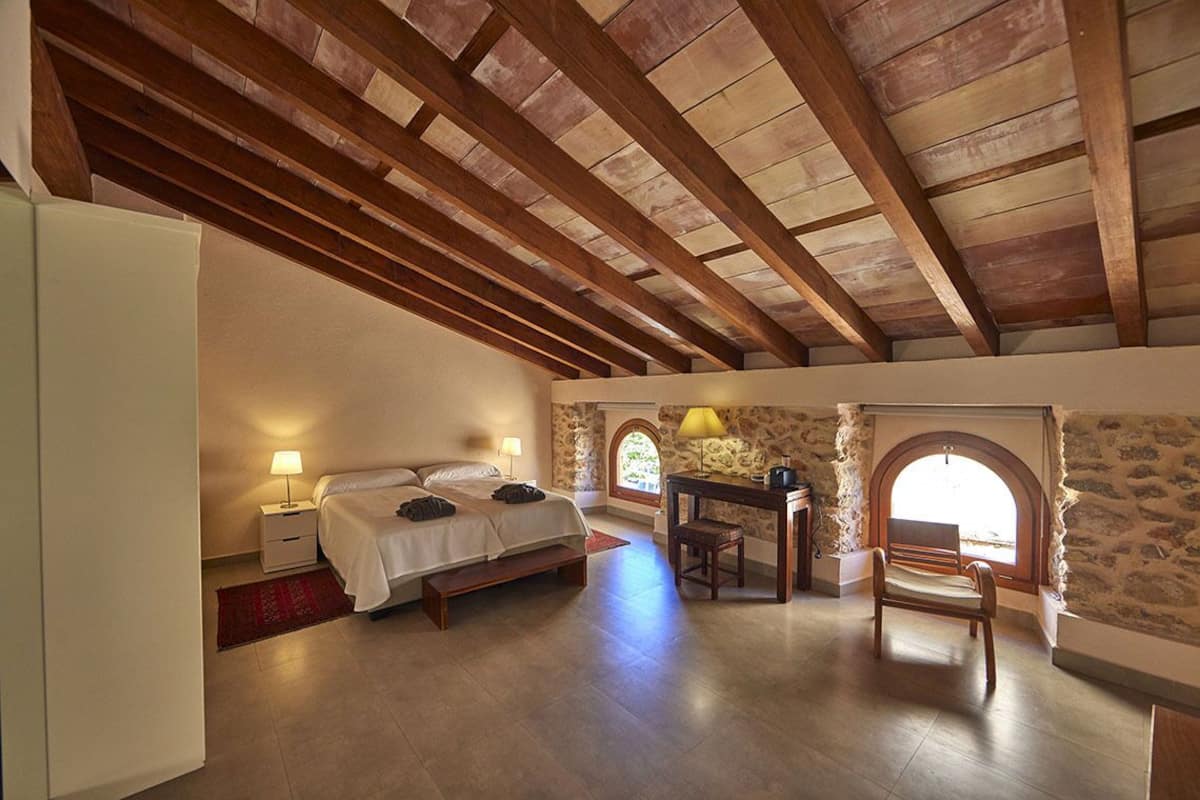 A bedroom with a wooden ceiling, a bed, a desk, and a chair.