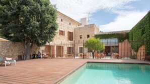 Un espace piscine doté d’une terrasse en bois, de bâtiments en pierre et de coins salon extérieurs.