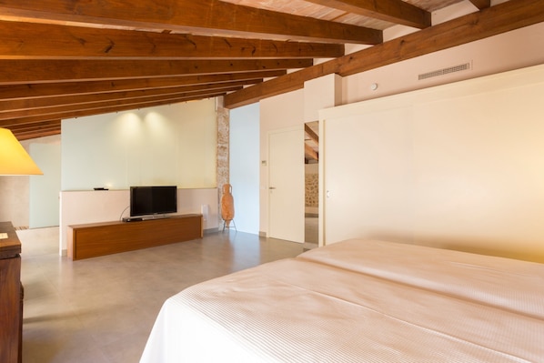 Un dormitorio con una cama grande, vigas de madera, un televisor y una pared de piedra.