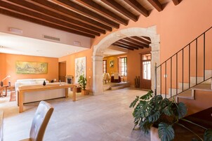 Amplia sala de estar con techo de madera, chimenea de piedra y escalera con barandilla de metal.