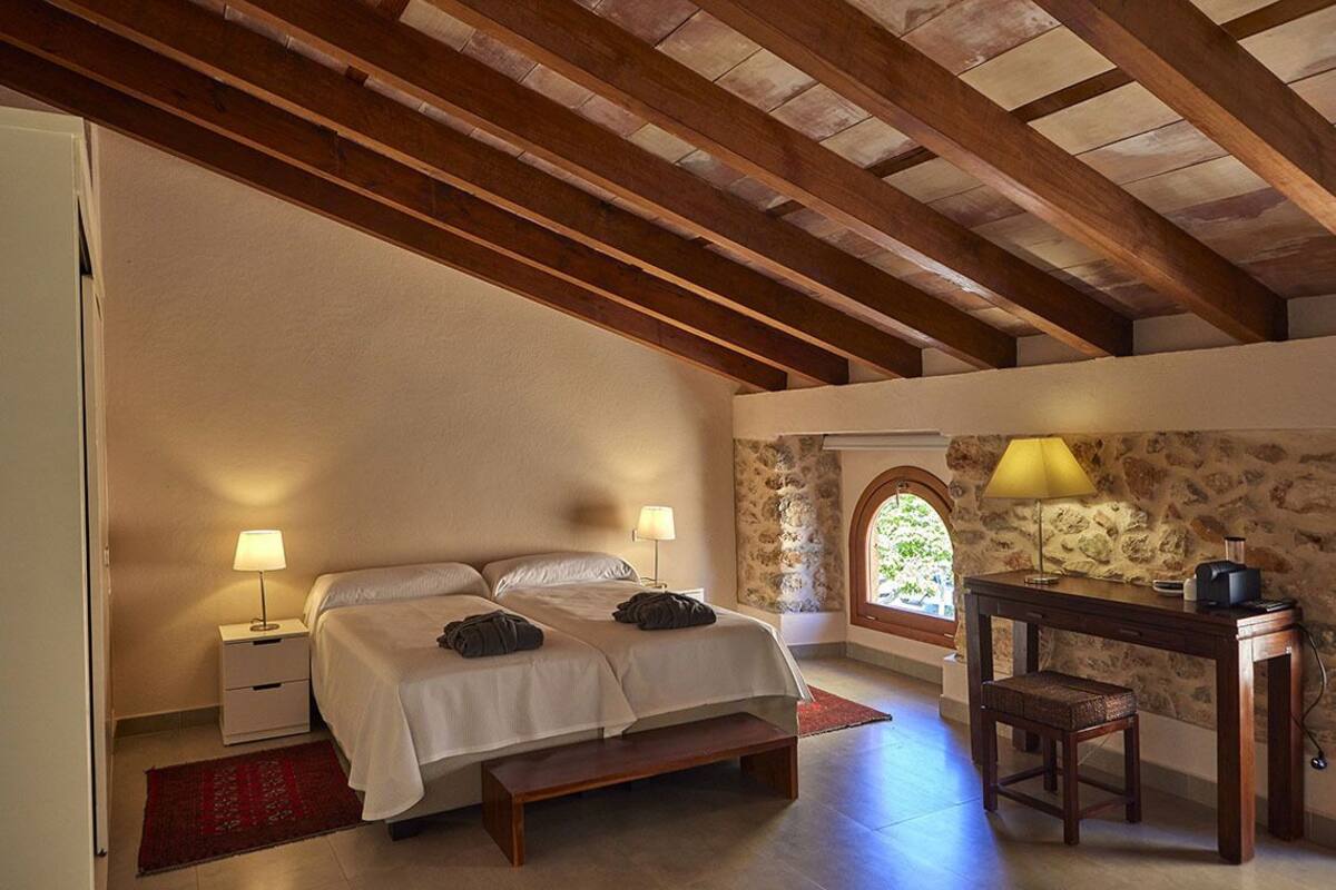 A bedroom with a bed, bedside tables, a desk, and a stone wall.