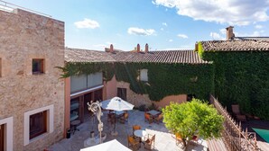 Un bâtiment en pierre avec un toit en tuiles, un espace extérieur aménagé pour s’asseoir et une piscine.
