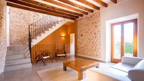 Un salon spacieux avec un mur en pierre, un escalier en bois, un canapé blanc et une table basse en bois.