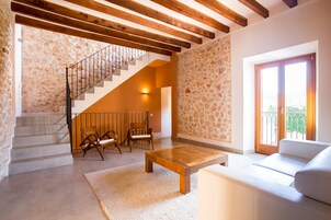 Un salón espacioso con pared de piedra, una escalera de madera, un sofá blanco y una mesa de centro de madera.