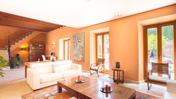Amplia sala de estar con un sofá blanco, una mesa de centro de madera y una escalera que conduce a un nivel superior.