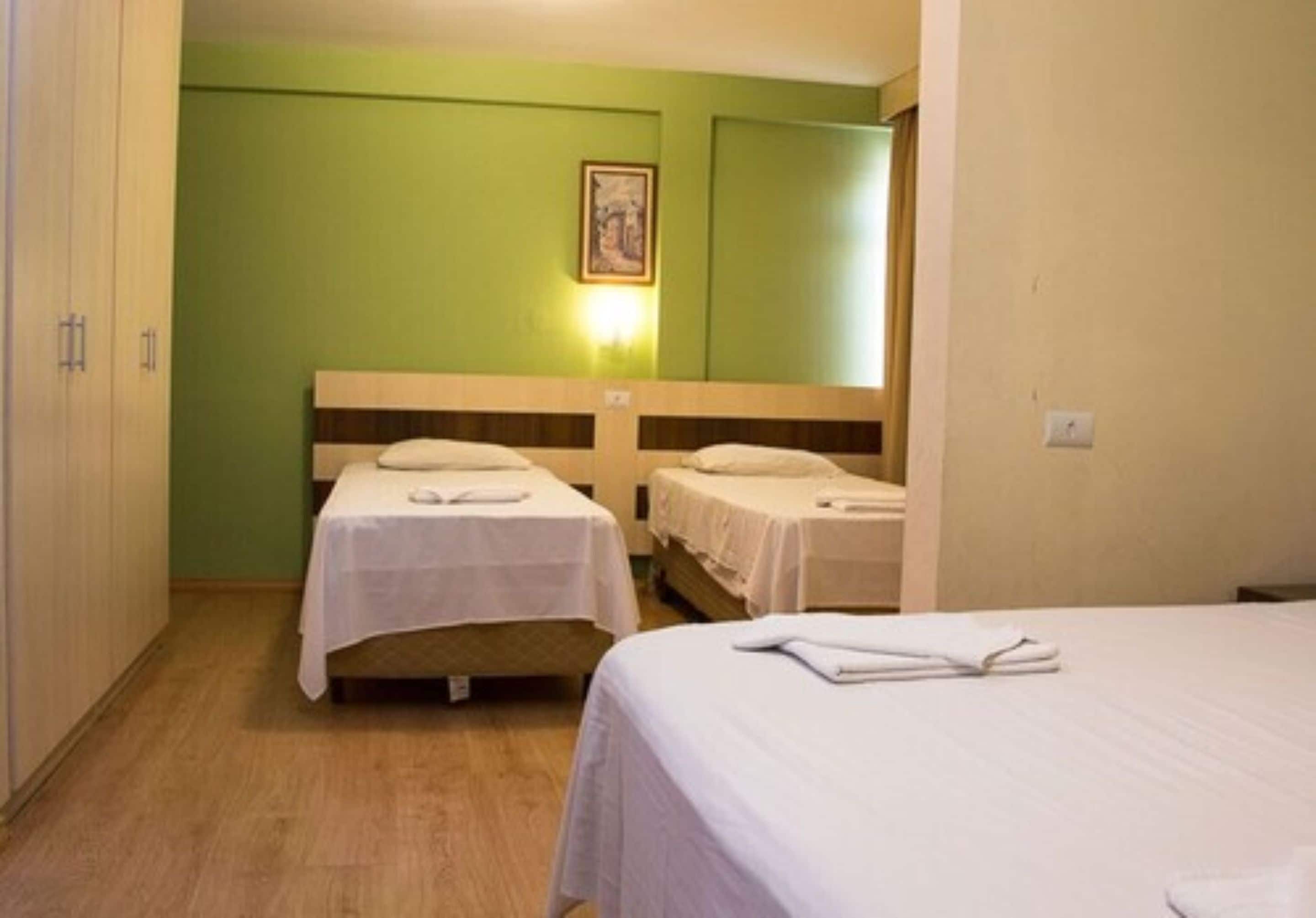 A hotel room with two single beds, a wooden headboard, a green wall, and a framed picture above the beds.