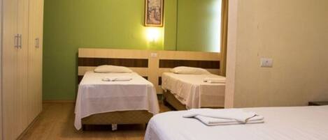A hotel room with two single beds, a wooden headboard, a green wall, and a framed picture above the beds.