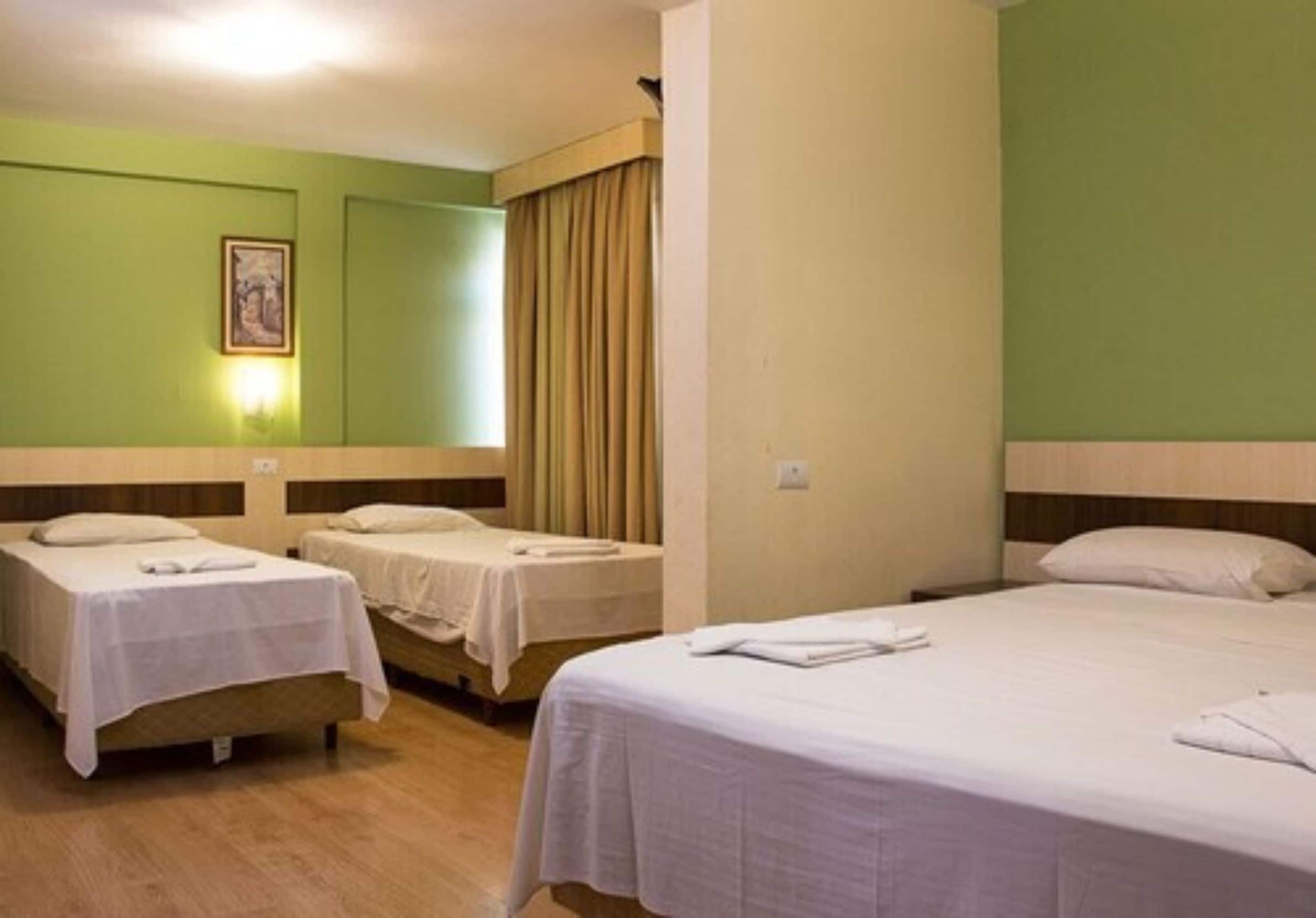Una habitación de hotel con dos camas individuales, una cama grande, una pared verde y un cuadro.