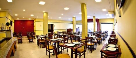A spacious dining area with multiple tables and chairs, a counter with a display, and a red door in the background.