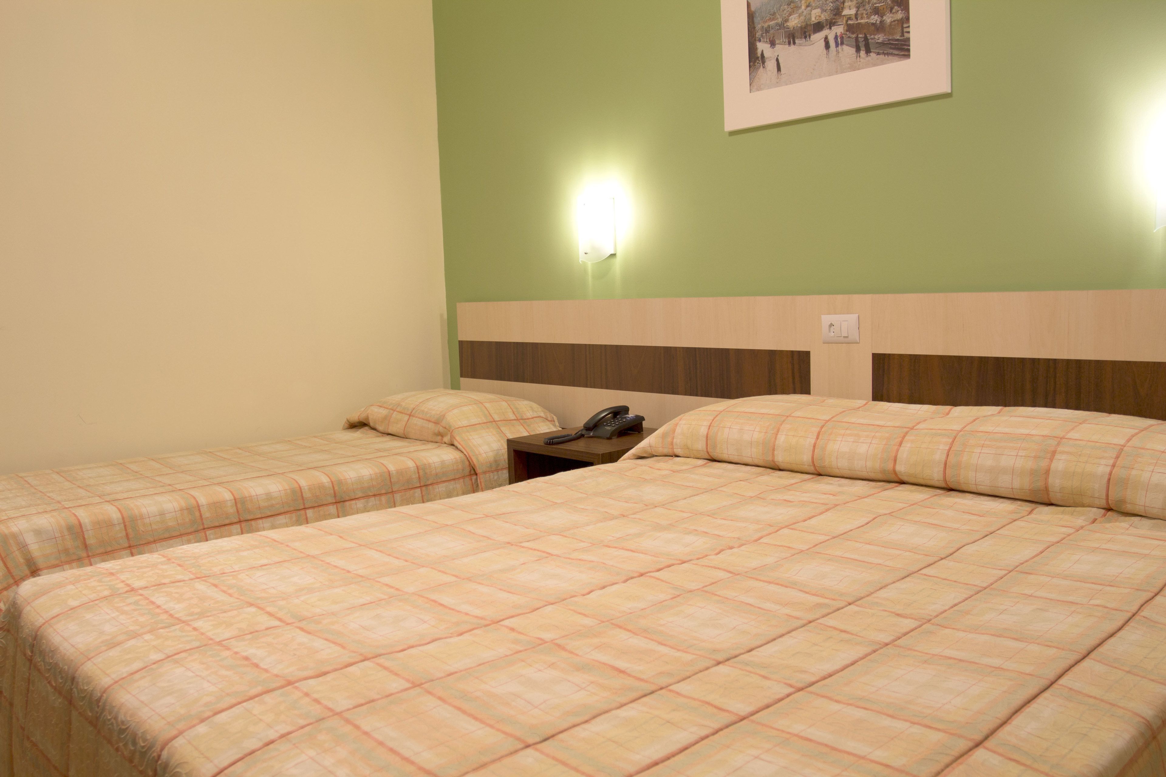 A hotel room with two beds, a nightstand, a telephone, and a wall-mounted light fixture.