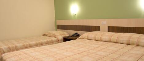 Habitación de hotel con dos camas, una mesita de noche, un teléfono y una lámpara fijada a la pared.
