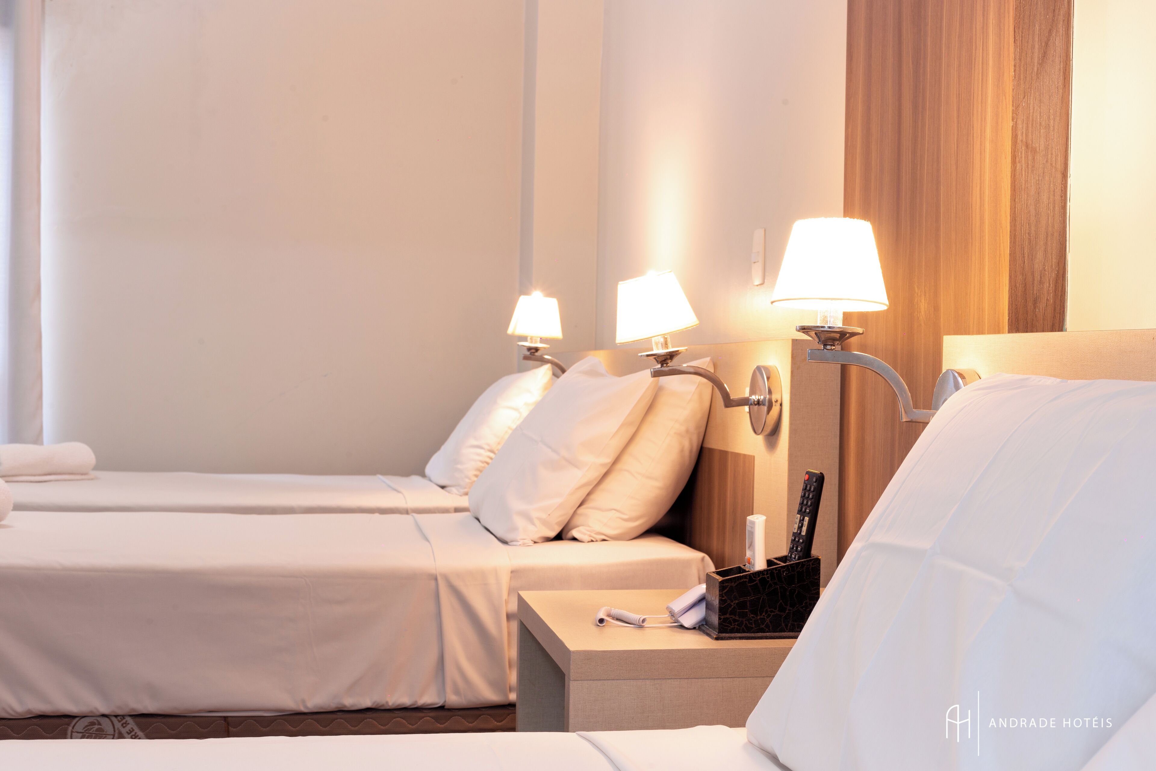 Habitación de hotel con dos camas, cada una con ropa de cama blanca y una mesita de noche con lámpara y control remoto.