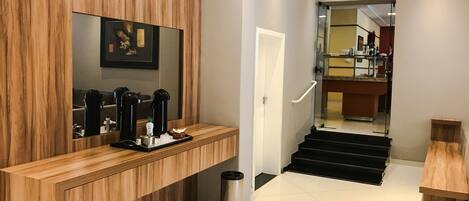 A modern hotel lobby with a wooden reception desk, a coffee machine, and a trash bin.