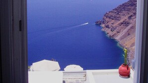 A view of the sea from a window, with a rocky coastline and a small boat in the distance. - Hotel Mylos (Santorini)