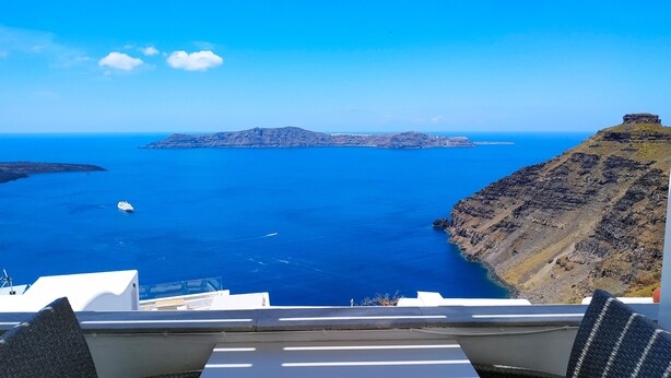 A view from a balcony overlooking a coastal landscape with a ship in the water and a rocky island in the distance. - Hotel Mylos (Santorini)