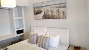 A bedroom with a white headboard, a painting of a snowy landscape, and a bedside table with a lamp. - Hotel Mylos (Santorini)