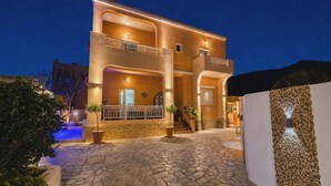 Un edificio de dos pisos con patio empedrado, balcones e iluminación exterior.