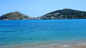 Un paisaje costero con aguas azules cristalinas, una playa de guijarros y una colina con edificios.