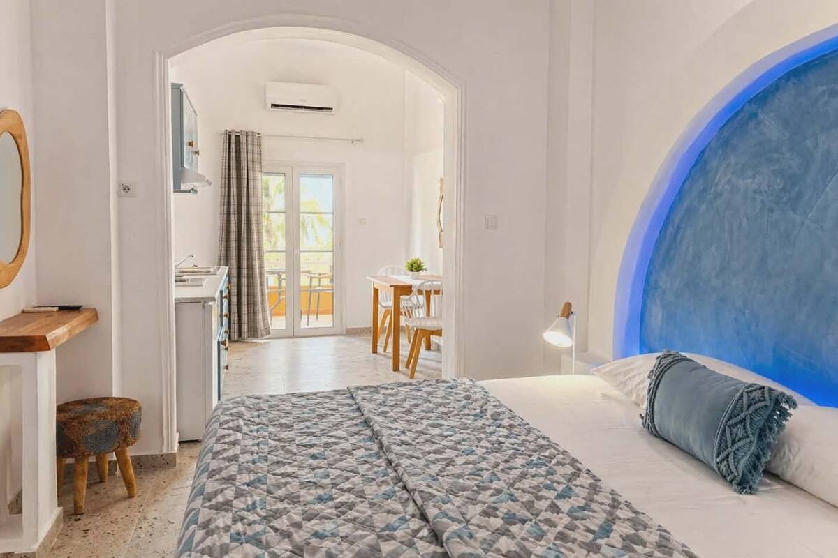 A bedroom with a large bed, a desk, a chair, and a view of the balcony.
