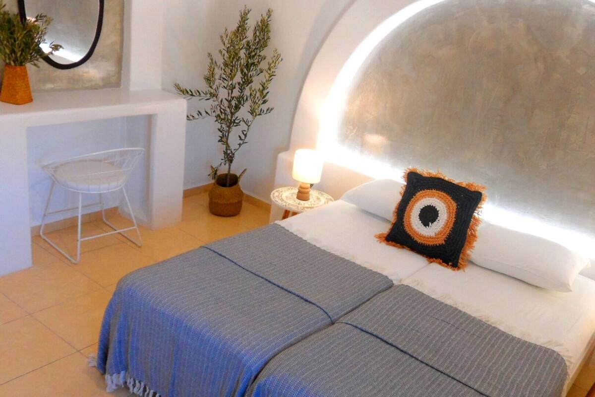 A modern bedroom with a large bed, a small desk, and a potted plant.