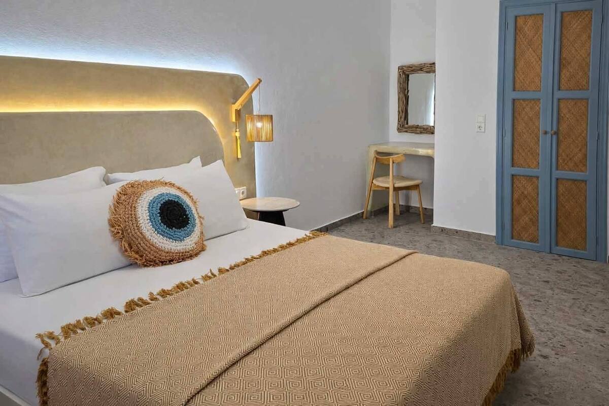 A hotel room with a large bed, a bedside table, a chair, a mirror, and a wardrobe.