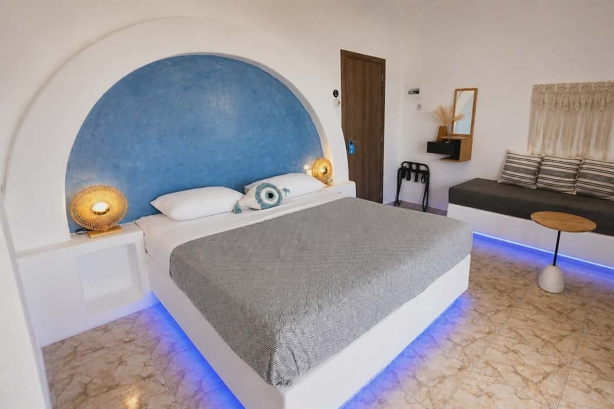 A bedroom with a bed, a sofa, a small table, and a wall-mounted TV.