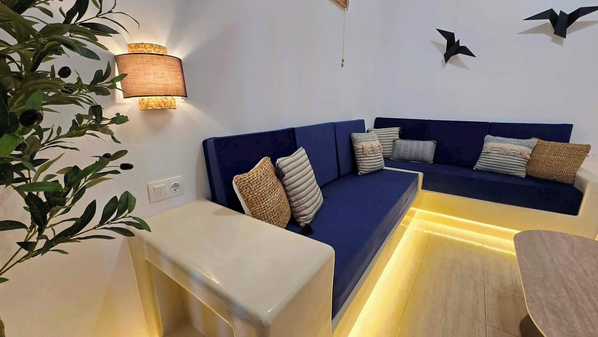 A modern living room with a blue sofa, decorative pillows, a side table, and a wall-mounted lamp.