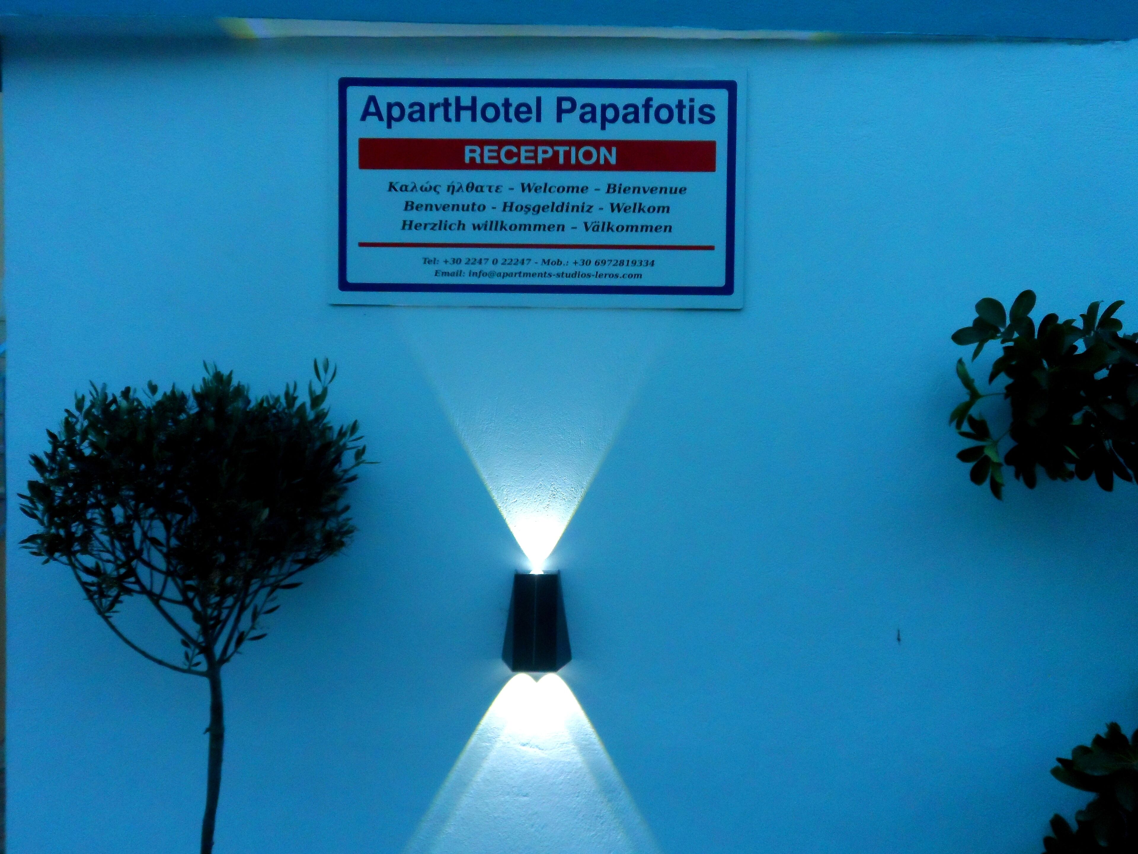 A reception sign for ApartHotel Papafotis with multilingual welcome messages and contact information.