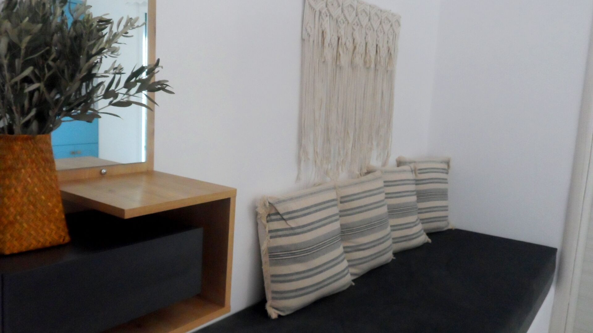 A room with a wooden console table, a potted plant, a dark sofa, and striped cushions.