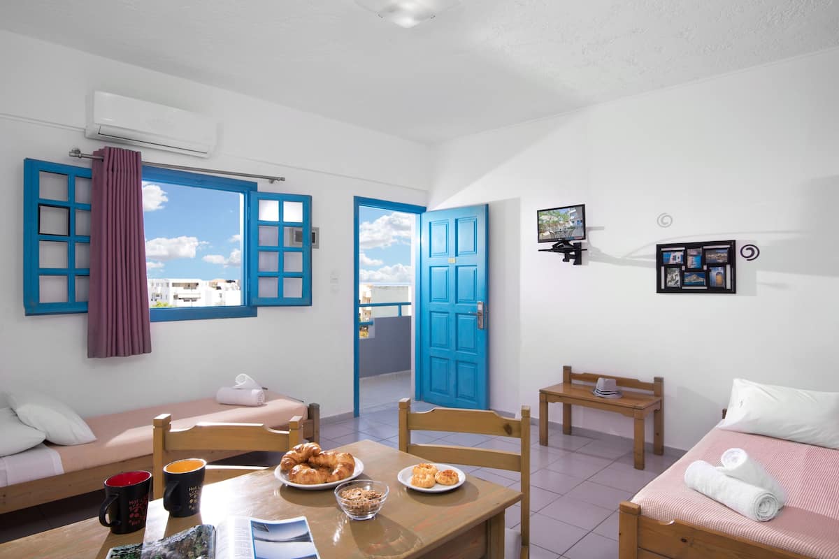 A compact room with a bed, a small table with breakfast items, a chair, and a TV on the wall.