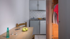 A compact kitchen with a dining table, a small refrigerator, and a wooden cabinet. - Erofili Apartments (Hersonissos)