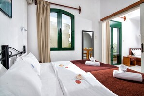 A hotel room with two beds, a large window with curtains, a mirror, a wooden door, and a small table with a chair. - Erofili Apartments (Hersonissos)