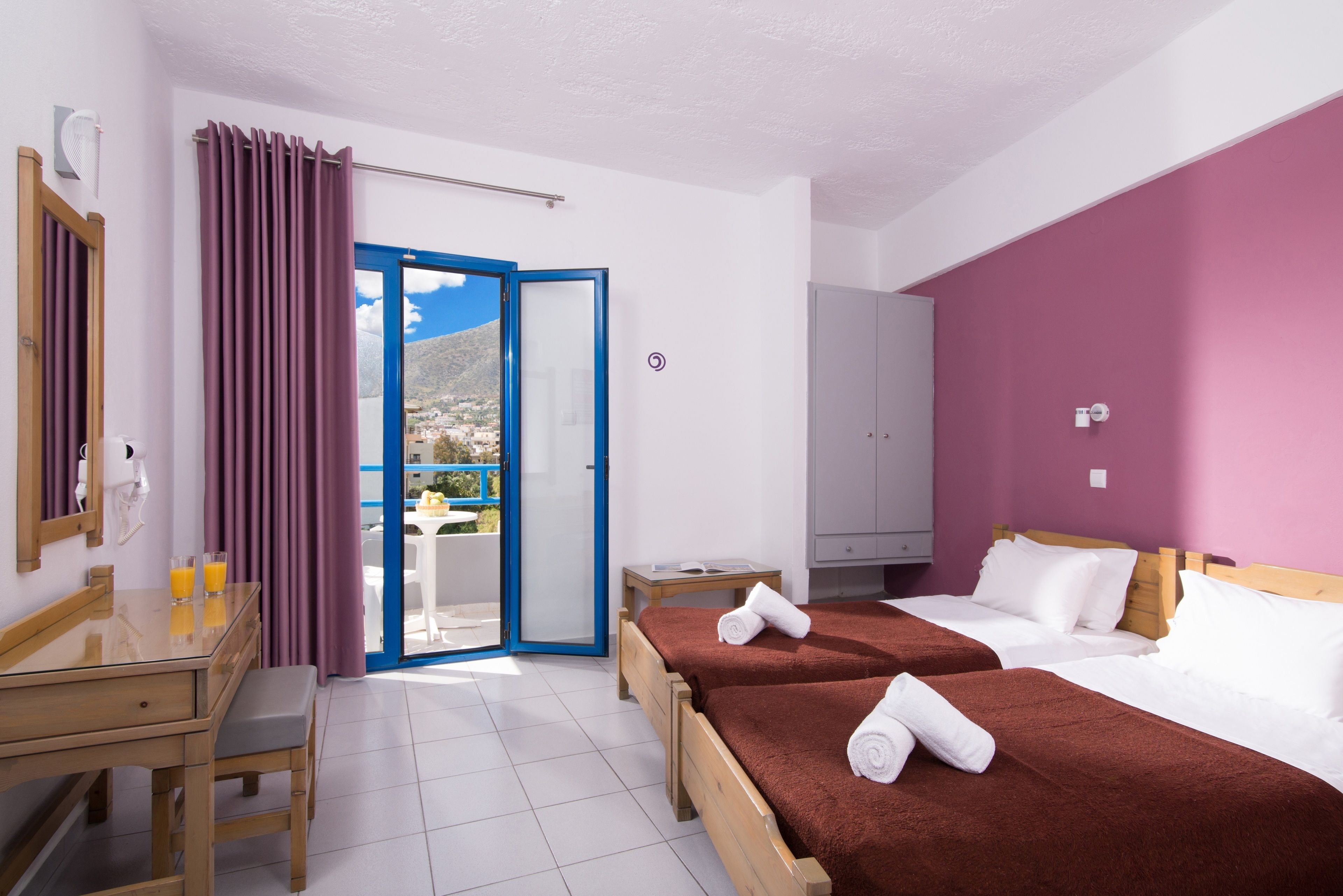 Habitación de hotel con dos camas, un escritorio con silla, una mesita y un armario.