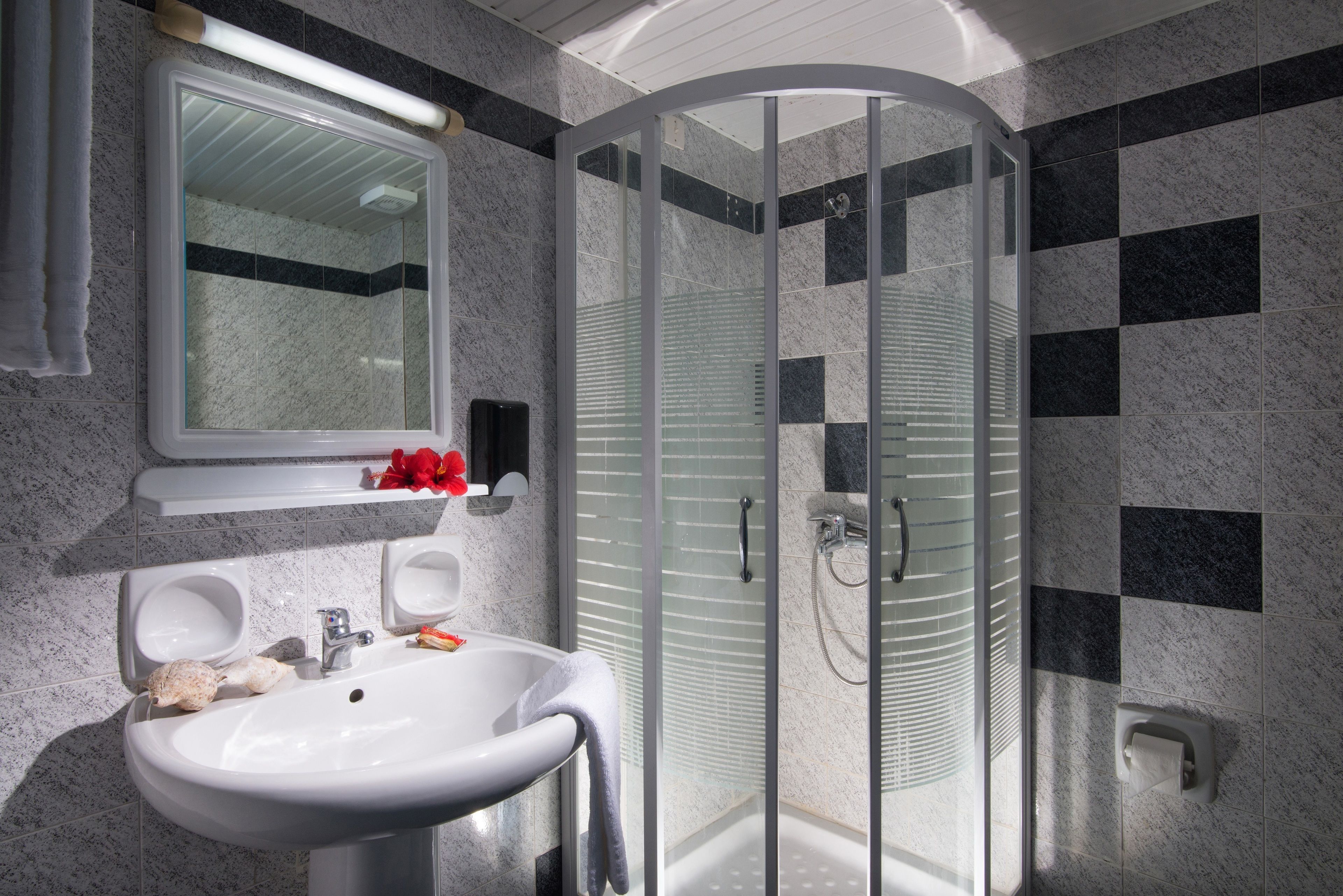 A modern bathroom with a glass-enclosed shower, a white sink with a mirror above it, and a towel hanging on the wall.