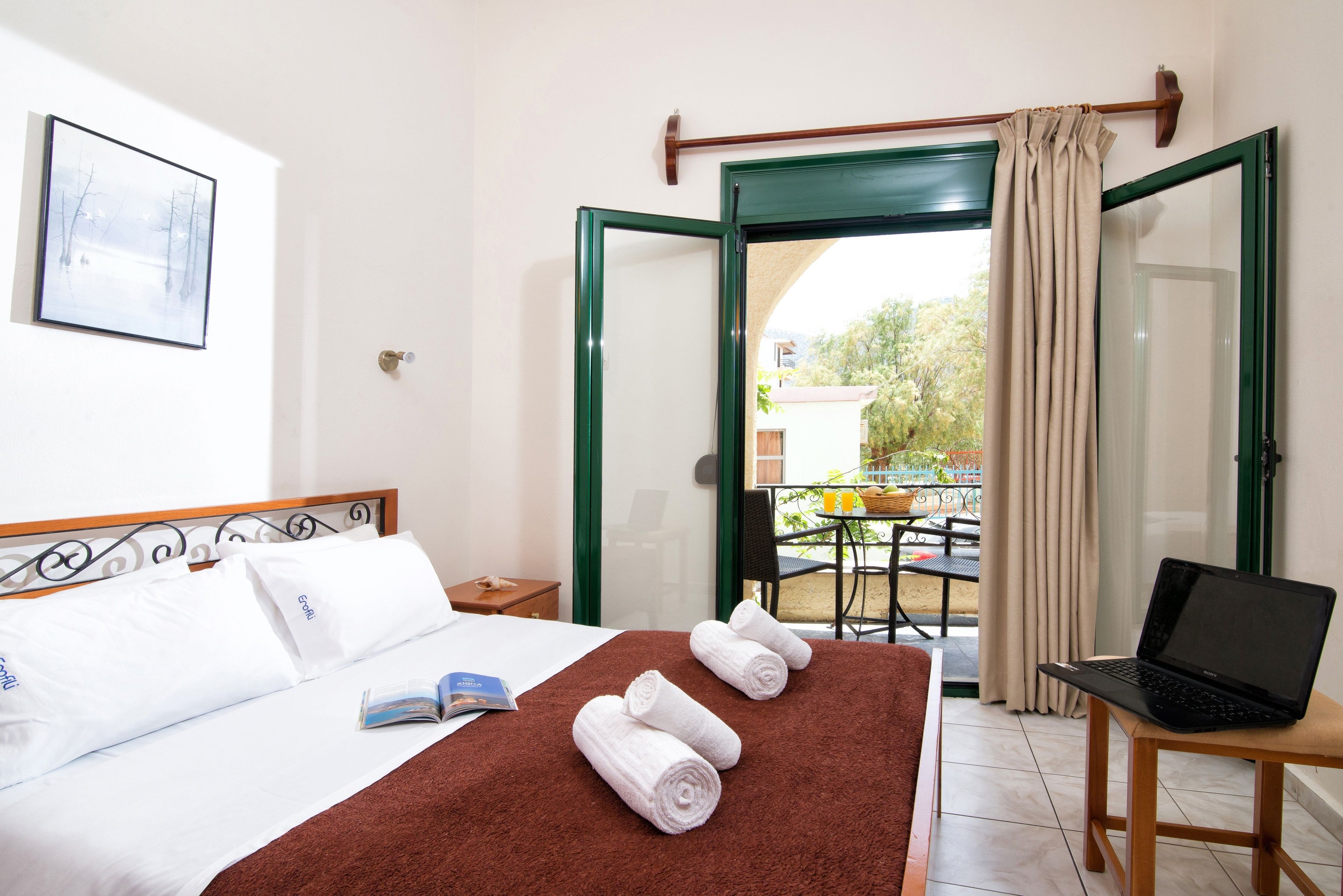 A hotel room with a bed, a laptop on a table, and a view of the outside.