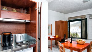 A compact kitchen with a coffee maker, kettle, and a dining area with a table and chairs. - Erofili Apartments (Hersonissos)