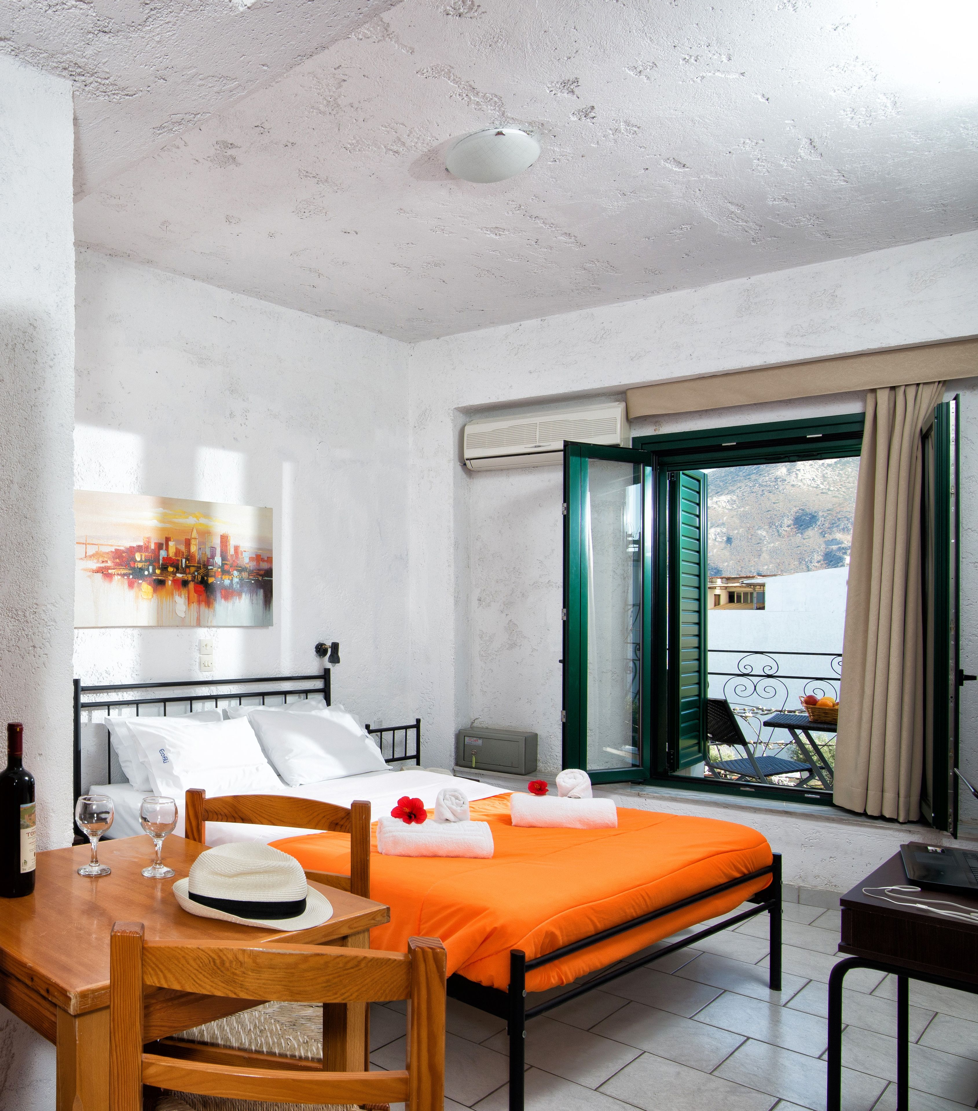 Habitación de hotel con cama, una mesa de comedor con sillas, un cuadro en la pared y vista a través de una puerta abierta.