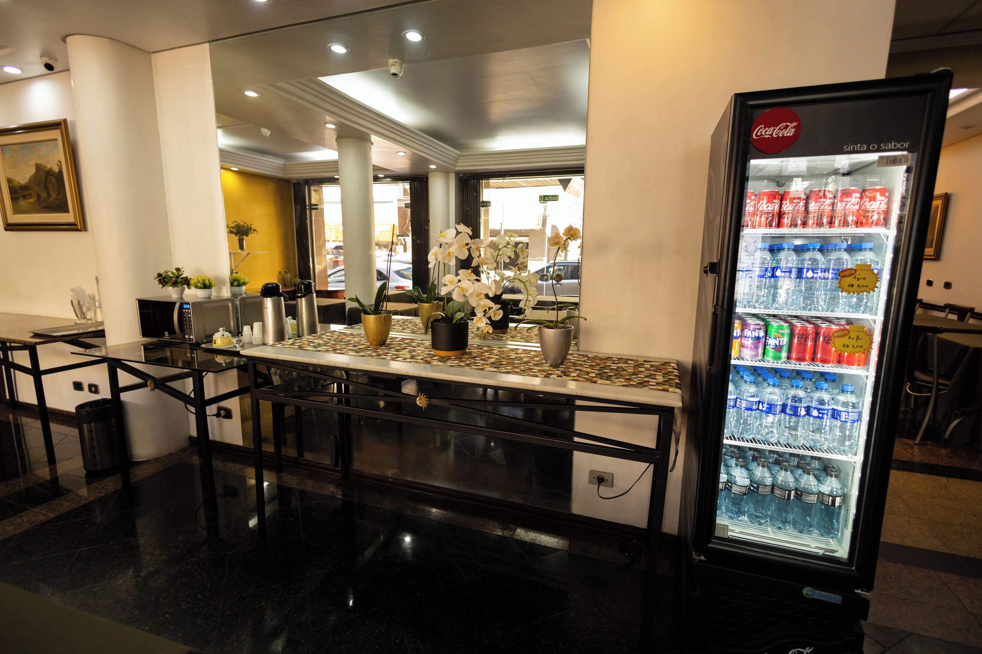 Eine Hotelhalle mit einem Coca-Cola-Kühlschrank voller Getränke, einer Bar mit einer Kaffeemaschine und einer Sitzecke mit Stühlen und einem Tisch.