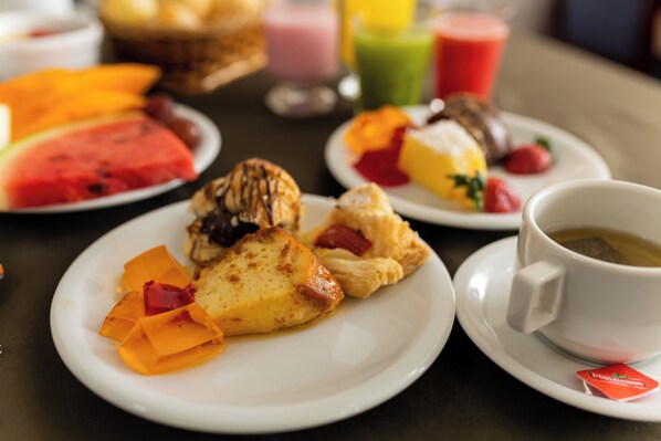 Una escena de desayuno con diversos pasteles, frutas y una taza de té sobre una mesa.