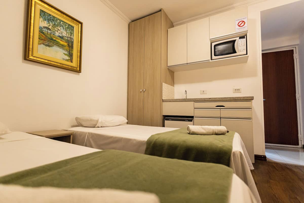 A hotel room with two beds, a painting, a microwave, and a kitchenette.