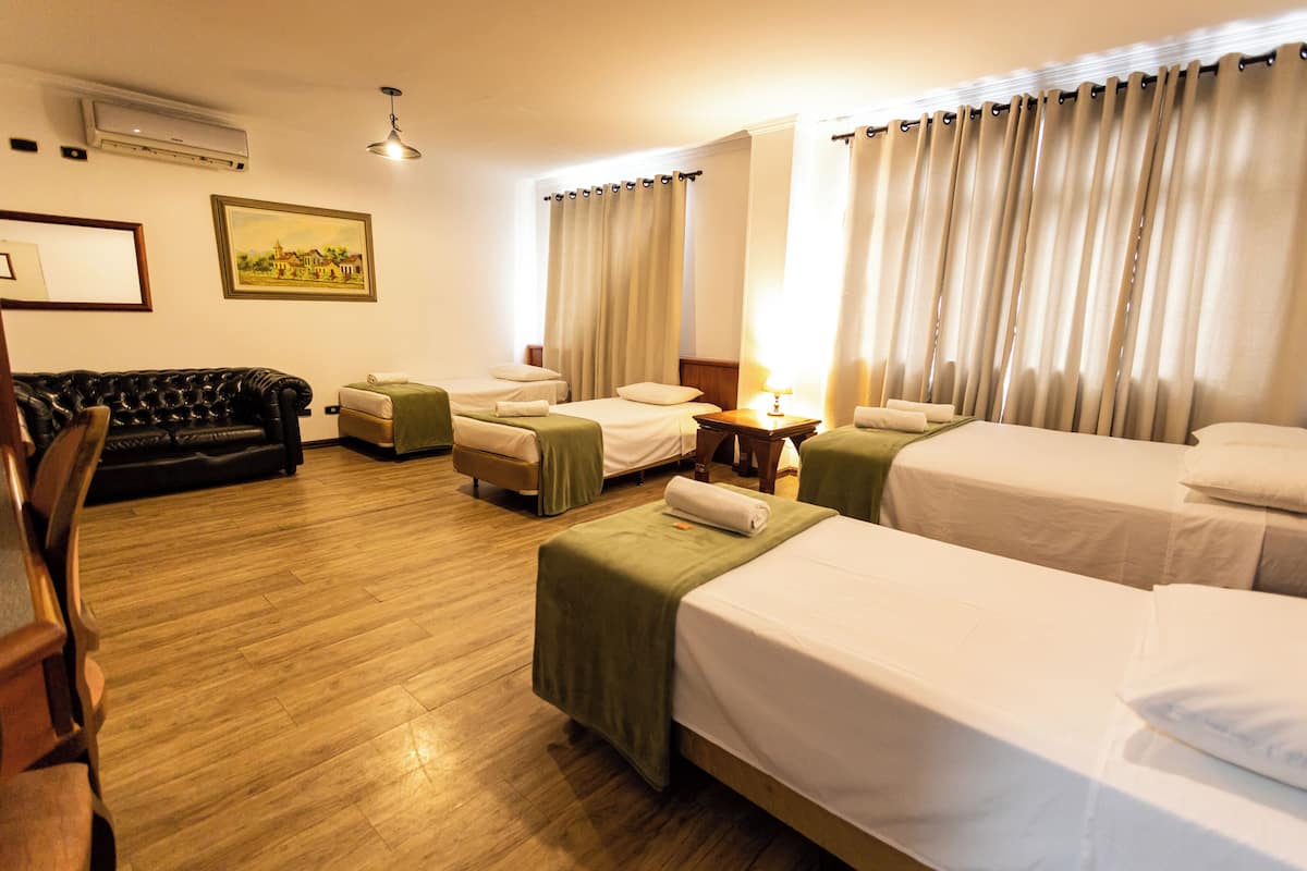 A hotel room with two single beds, a sofa, a chair, and a small table with a lamp.